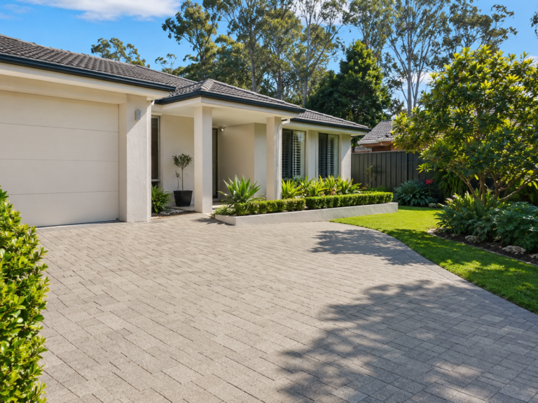 Front view of a freshly cleaned paved driveway at a Menai NSW home, with a neat garage, tidy entrance, landscaped garden beds, green lawn and surrounding trees.